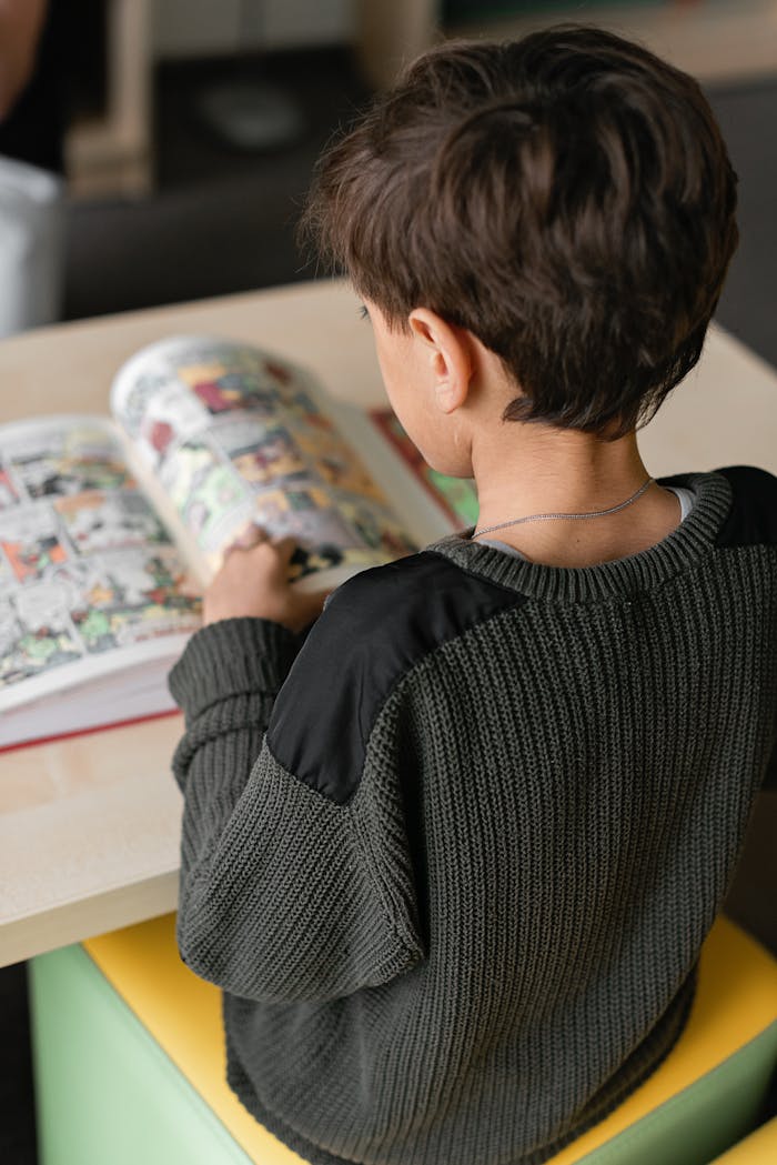 Young boy sitting indoors reading a colorful comic book.